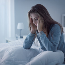 woman sitting on her bed while holding her head