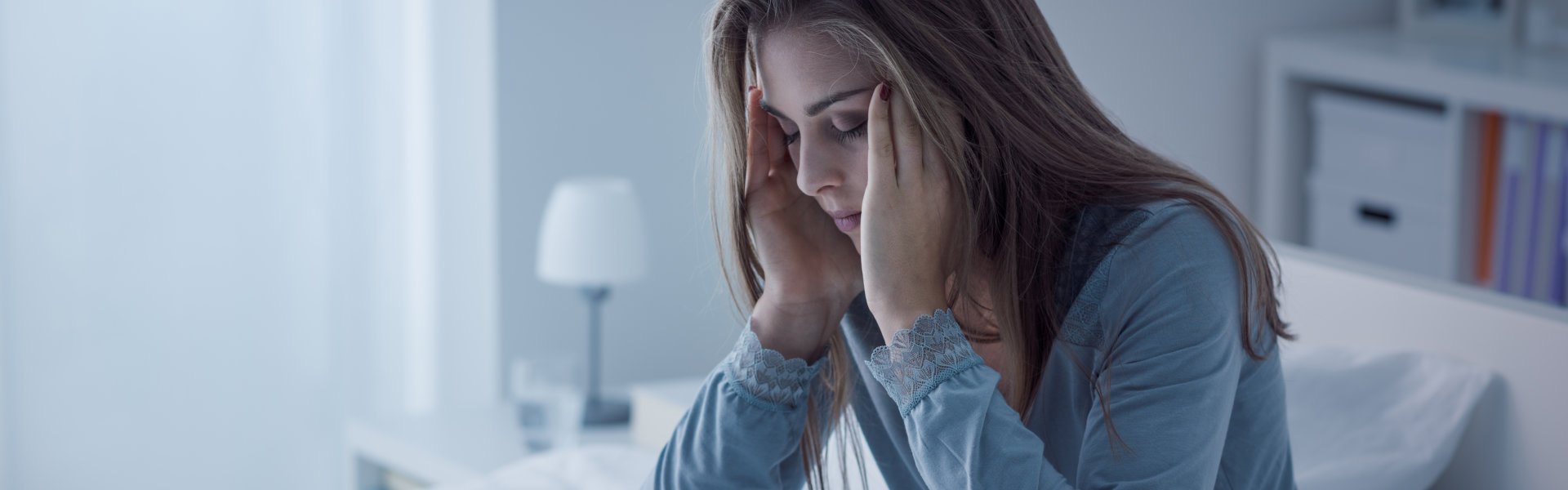 woman sitting on her bed while holding her head